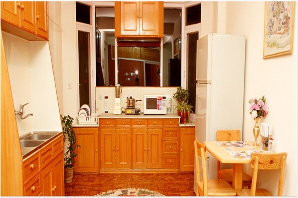 A compact kitchen with wooden cabinets, a microwave, a sink, and a dining area with a table and chairs. - Himalaya Apartment Hotel (Lalitpur)