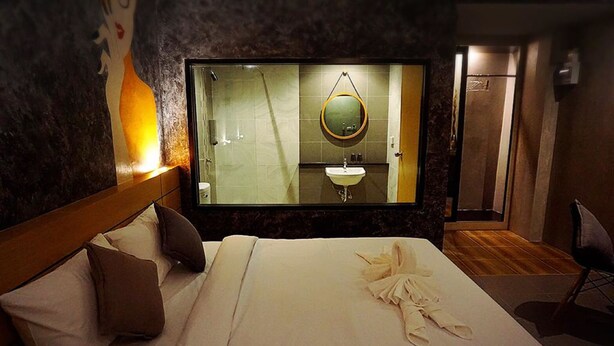 Een hotelkamer met een groot bed, hoofdeinde, nachtkastje, spiegel en uitzicht op de badkamer.