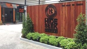 Een houten bord met 'HIDE & SEEK RESORT' en een receptie met een 'OUT'-bordje.