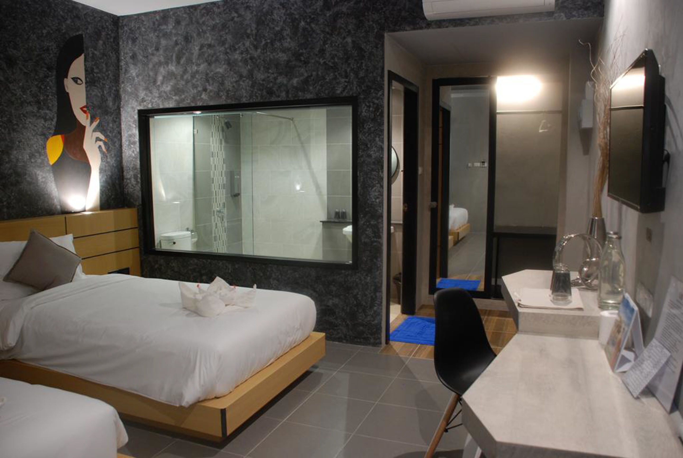 A modern hotel room with a large bed, a shower, a vanity with a mirror, and a wall-mounted TV.