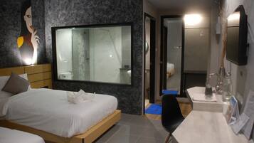 A modern hotel room with a large bed, a shower, a vanity with a mirror, and a wall-mounted TV.