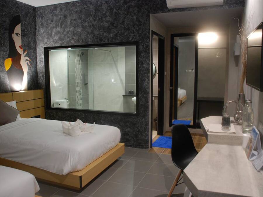 A modern hotel room with a large bed, a shower, a vanity with a mirror, and a wall-mounted TV.