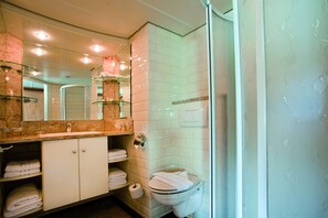 Une salle de bain dotée d’une douche à parois de verre, d’un lavabo avec un plan de toilette en marbre et de toilettes avec un abattant blanc.