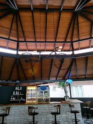 A covered outdoor seating area with a wooden ceiling and metal beams, a bar with stools, and a refrigerator. - Metin Hotel (Ortaca)