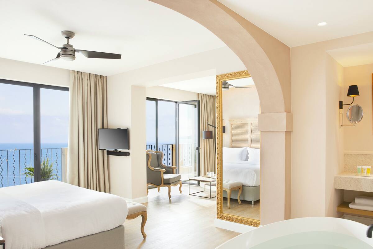 Habitación de hotel con cama, un espejo grande, bañera y balcón con vistas.