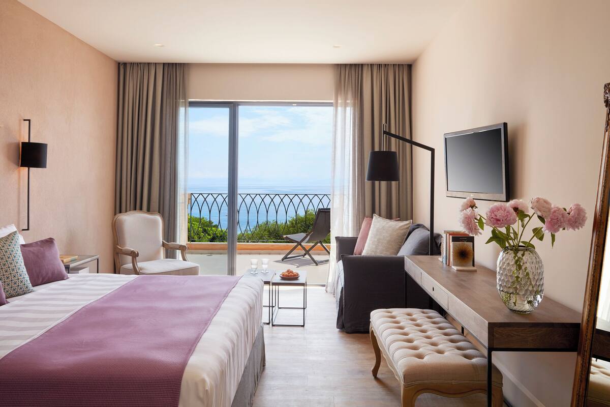 Habitación de hotel con cama, escritorio, silla, televisión y balcón con vista al mar.