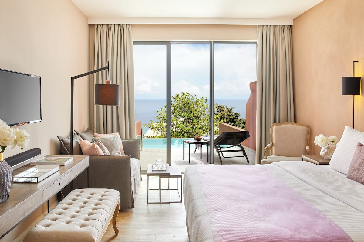 Habitación de hotel con una cama grande, un escritorio con computadora, una silla, televisor y vista al océano.