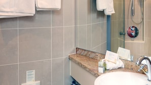 A modern bathroom with a large mirror, a sink, and a shower. There are multiple towels hanging on the wall and a soap dispenser on the counter. - Crossgates Hotelship Medienhafen - Düsseldorf (Düsseldorf)