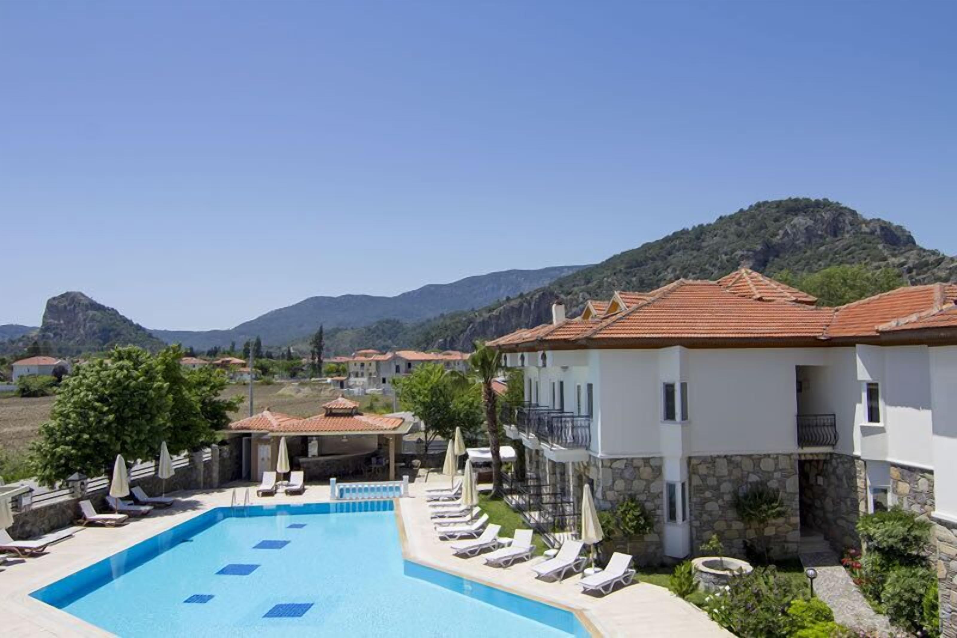 A resort with a swimming pool, lounge chairs, and a mountainous backdrop.