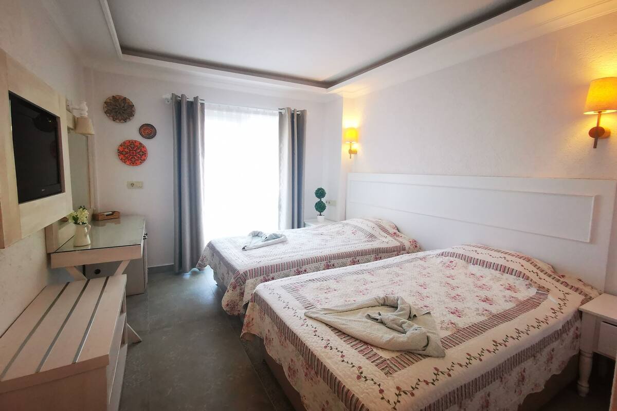 A hotel room with two beds, a desk, a TV, and a window with curtains.