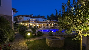 Un hotel con piscina, mobiliario exterior y un sendero de jardín bien iluminado.