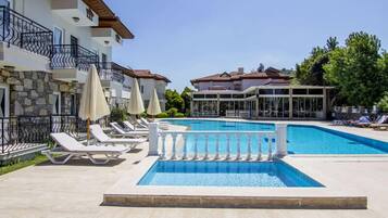Una piscina con sillones de playa y sombrillas, rodeada de edificios de varios pisos con balcones.