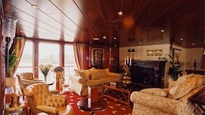 A spacious living room with a fireplace, leather armchairs, a coffee table, and a large window with curtains. - Crossgates Hotelship Medienhafen - Düsseldorf (Düsseldorf)