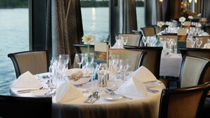 A dining area with tables set for dinner, overlooking a body of water. - Crossgates Hotelship Messe - Düsseldorf (Düsseldorf)