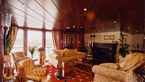 A spacious living room with a fireplace, leather armchairs, a coffee table, and a large window with curtains. - Crossgates Hotelship Messe - Düsseldorf (Düsseldorf)