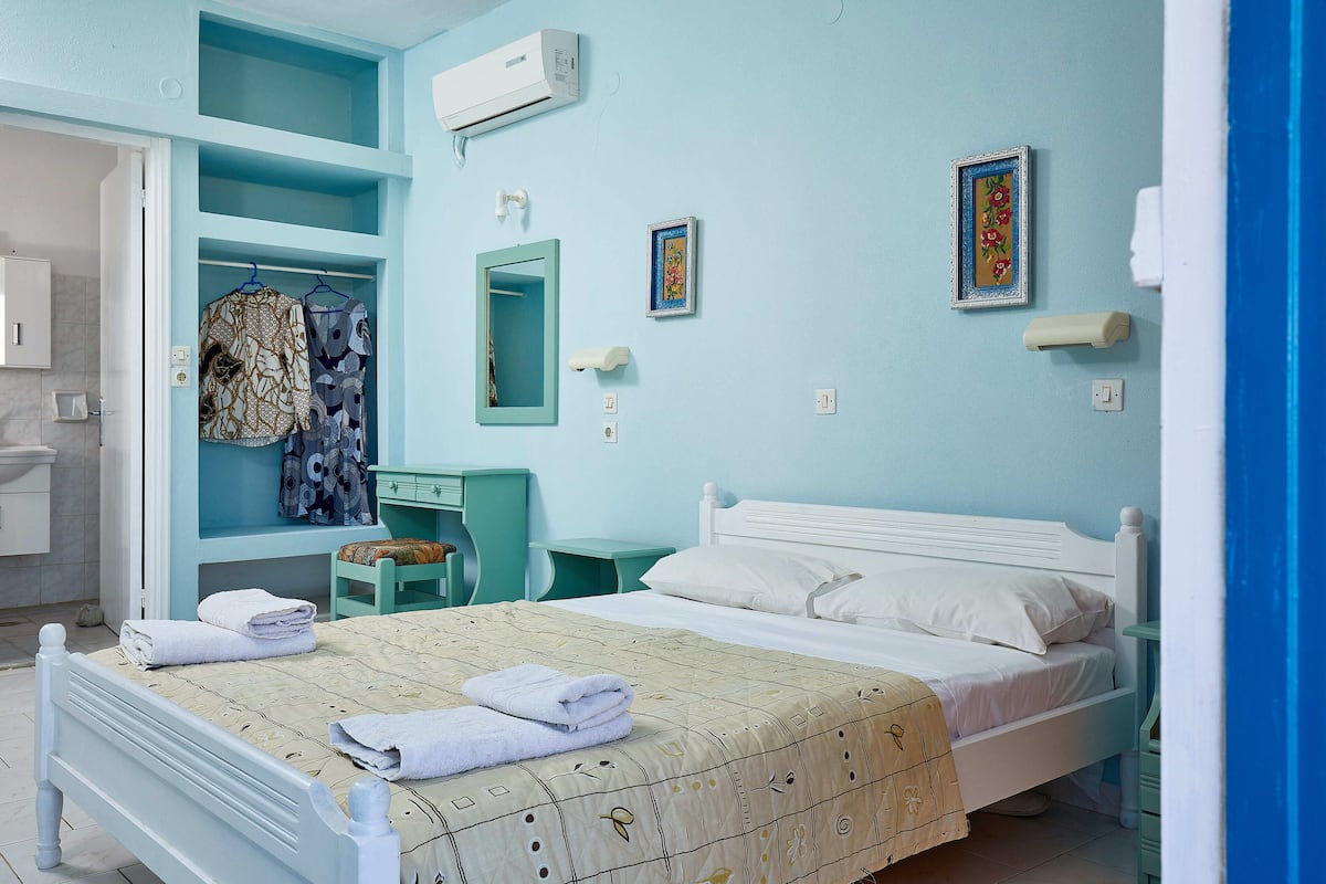 A bedroom with a bed, a wardrobe, a mirror, and a wall-mounted air conditioner.