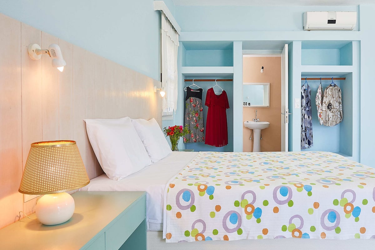 A bedroom with a bed, a nightstand, a lamp, a wardrobe, and a mirror.