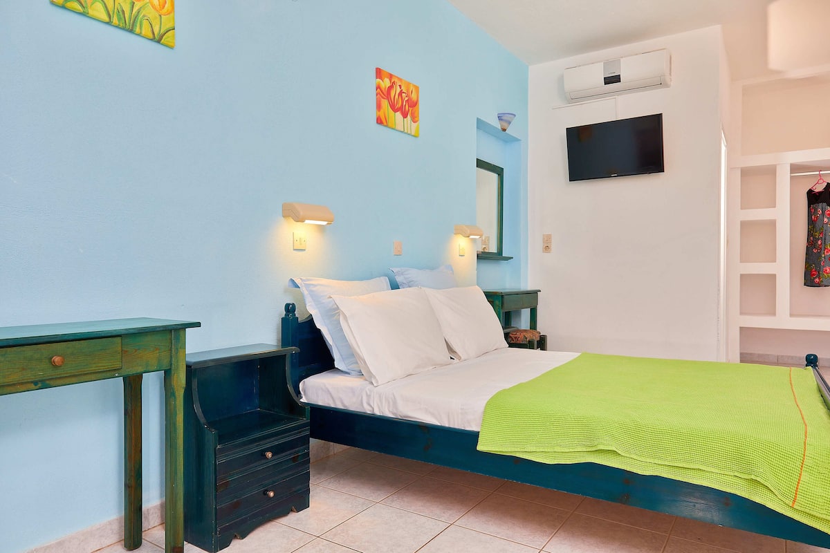 A bedroom with a bed, bedside tables, a dresser, a TV, and a wall-mounted air conditioner.