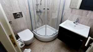 Un baño con ducha envuelta en vidrio, inodoro blanco y lavamanos con mueble negro.