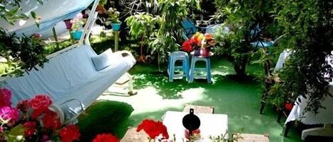 Een tuin met een witte stoel, een tafeltje en een blauwe kruk. Overal staan potten met planten en bloemen.