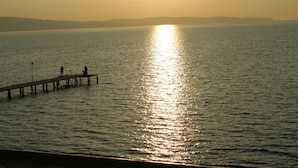 Un muelle se adentra en aguas tranquilas, con el sol reflejado en la superficie.