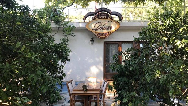Cómoda zona de estar al aire libre con una mesa y sillas, rodeada de abundante vegetación y un letrero decorativo arriba.