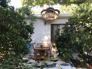 A cozy outdoor seating area with a table and chairs, surrounded by lush greenery and a decorative sign above. - Pekcan Otel (Burhaniye)