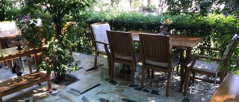 An outdoor patio with a mosaic floor, wooden furniture, and lush greenery.