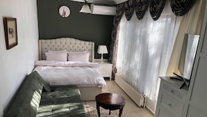 Un dormitorio con una cama grande, un sofá, una mesita, un aparador, una lámpara, un reloj y un radiador.