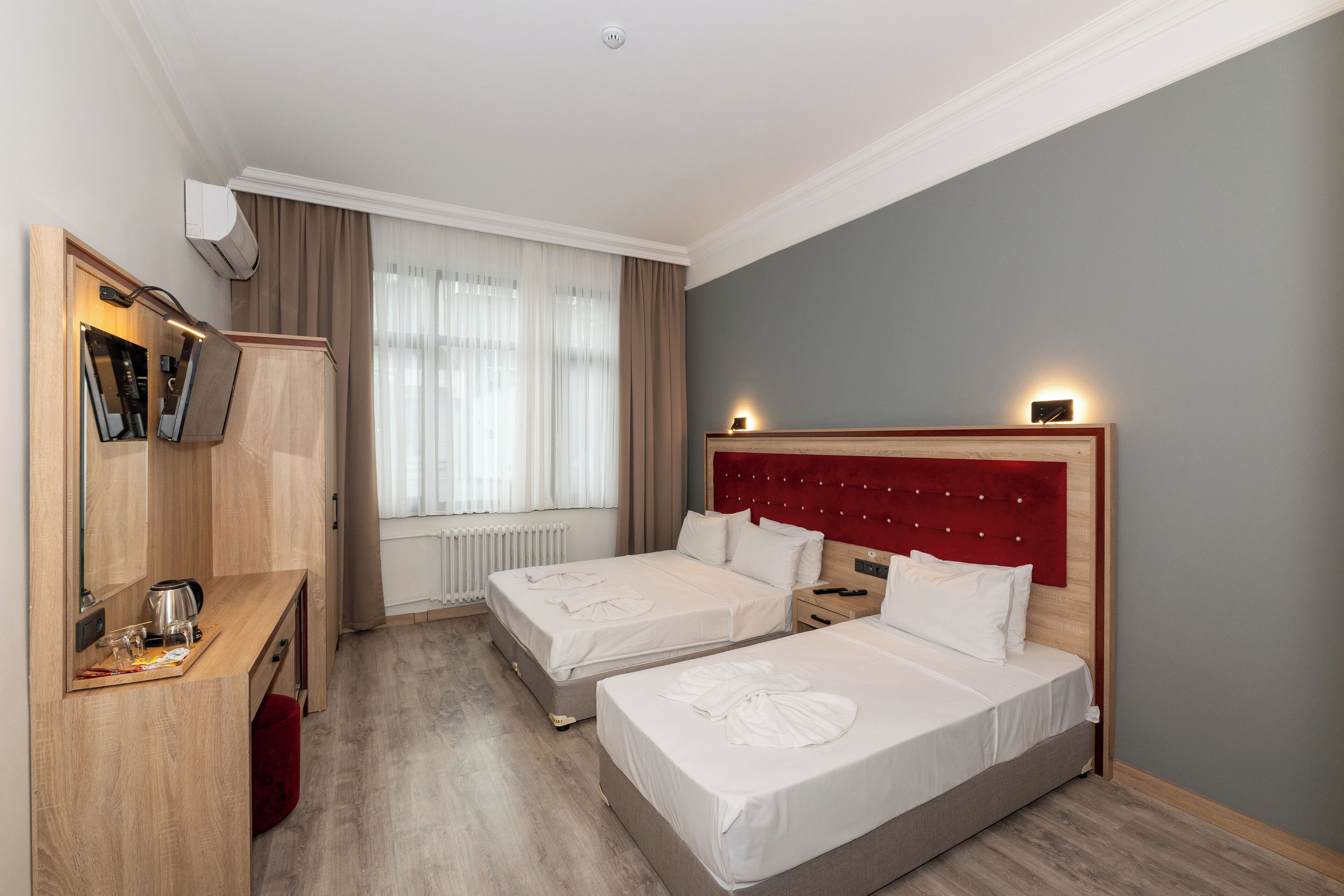 Quarto de hotel com duas camas, uma escrivaninha de madeira, televisão e janela com cortinas.