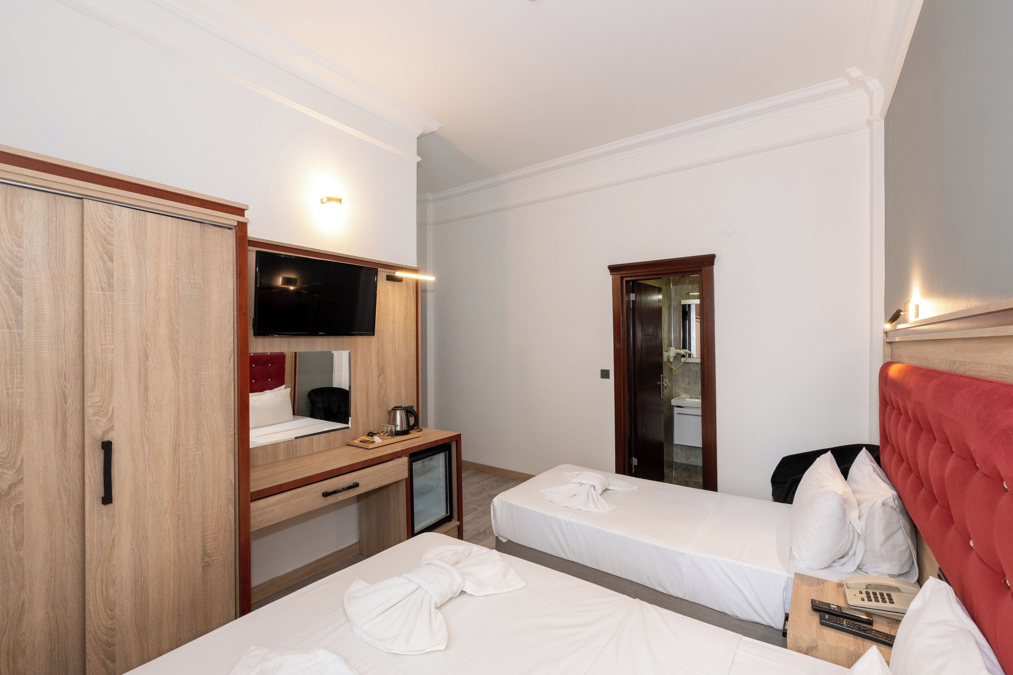 A hotel room with two beds, a desk with a TV, a minibar, and a red headboard.