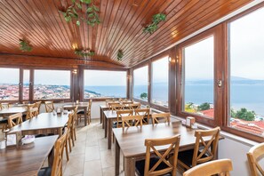 A restaurant with wooden tables and chairs, large windows with a view of the sea and town. - Olimpic Hotel (Istanbul)