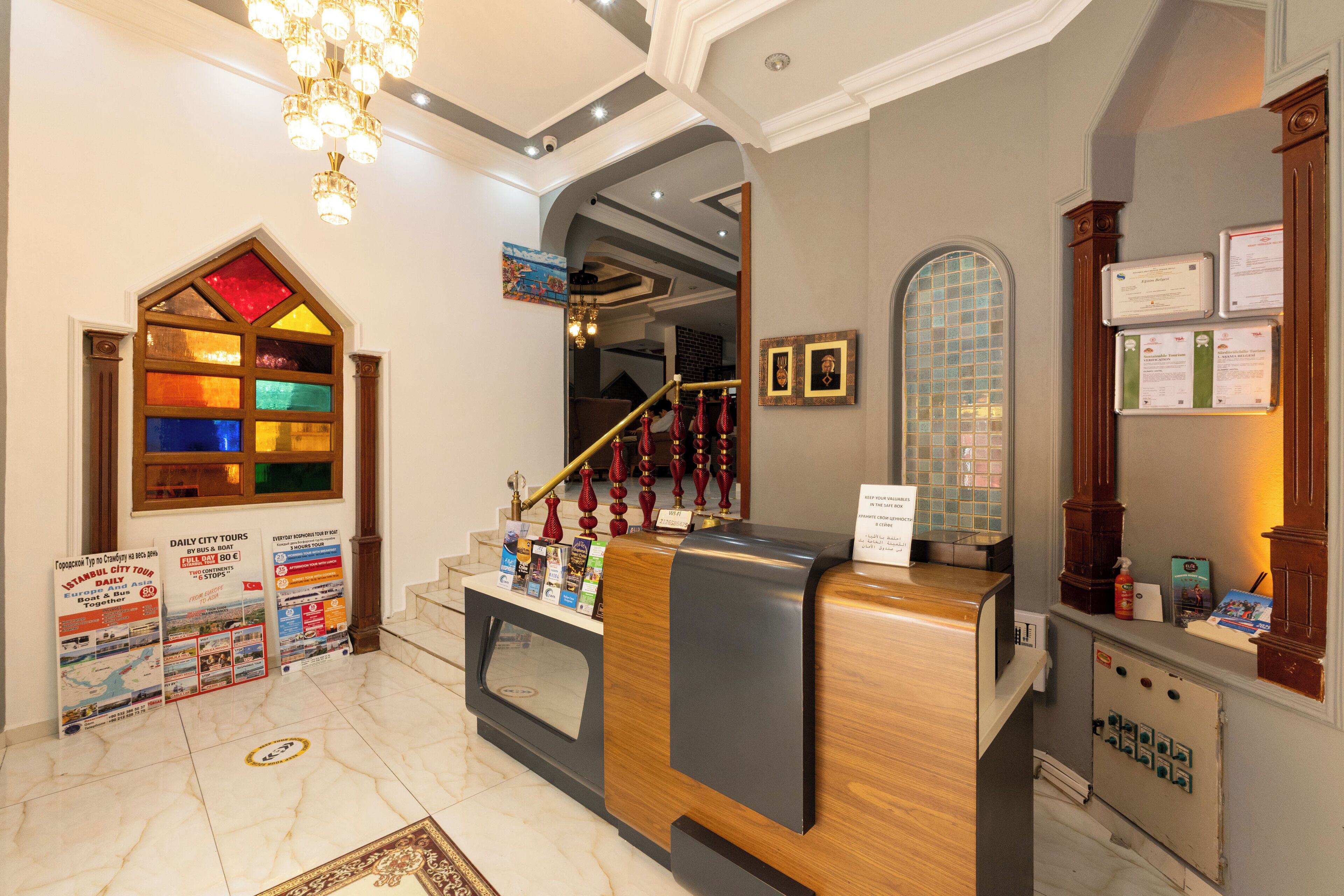 A reception area with a wooden reception desk, a chandelier, a staircase, and a wall with framed pictures and informational posters.