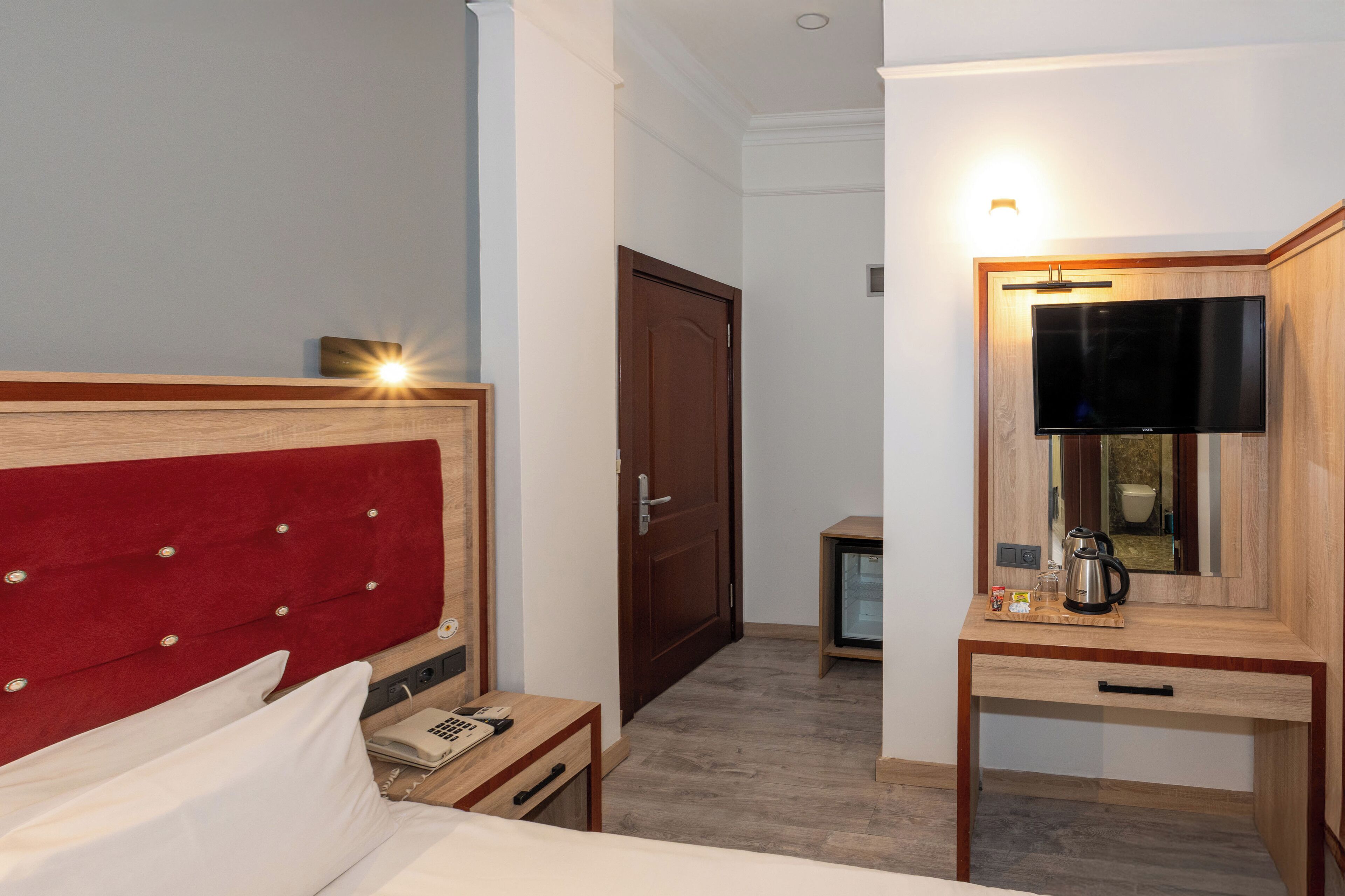 Une chambre d’hôtel comprenant un lit, une table de chevet avec un téléphone, une petite table avec une cafetière et un téléviseur fixé sur un meuble en bois.