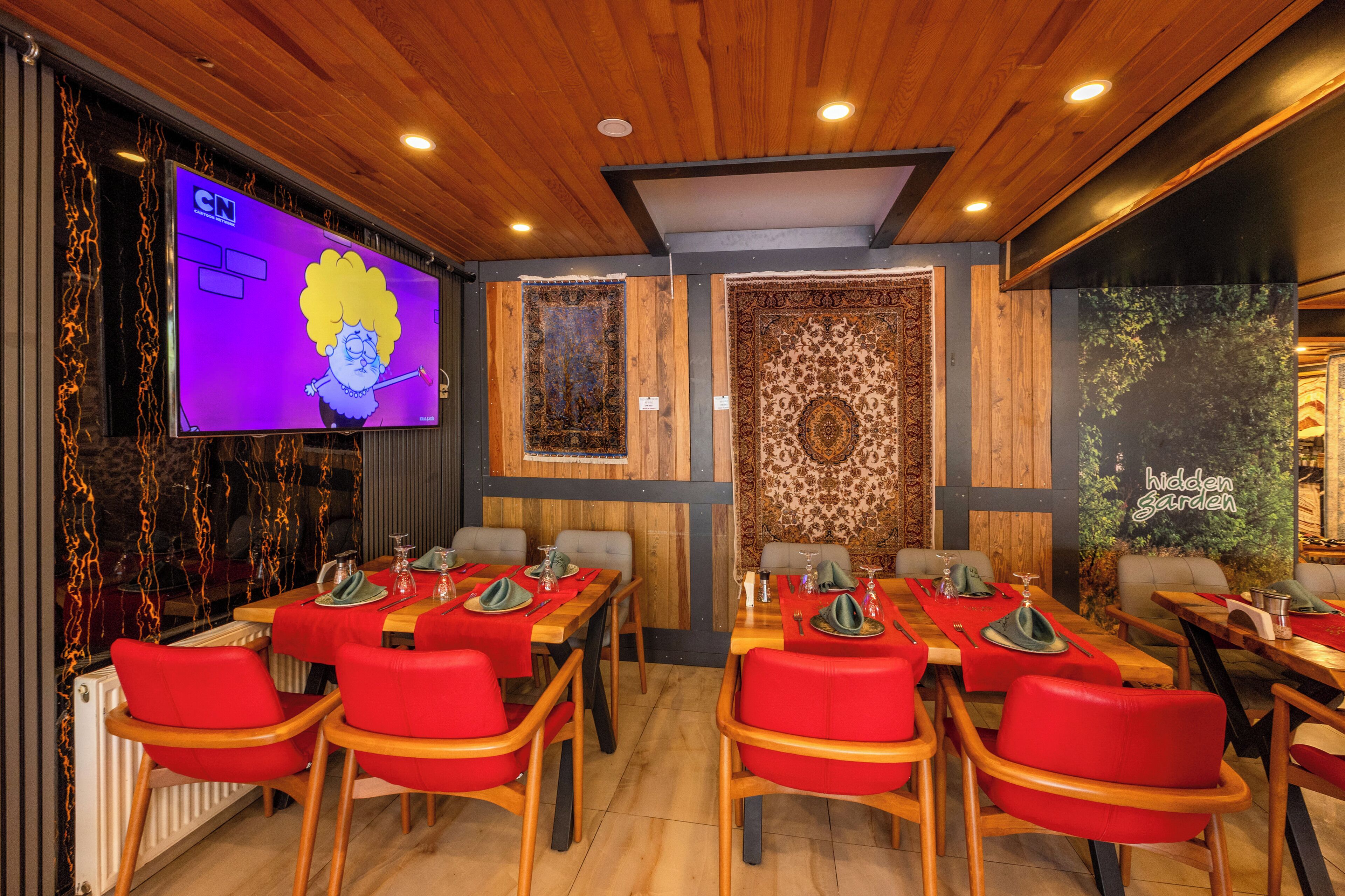 A restaurant with wooden ceiling and walls, red chairs, and tables set for dining.