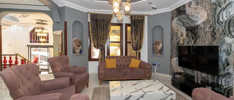 Amplia sala de estar con un sofá modular grande, una mesa de centro y un televisor de pantalla plana. La habitación cuenta con una pared con diseño de mármol y un candelabro.