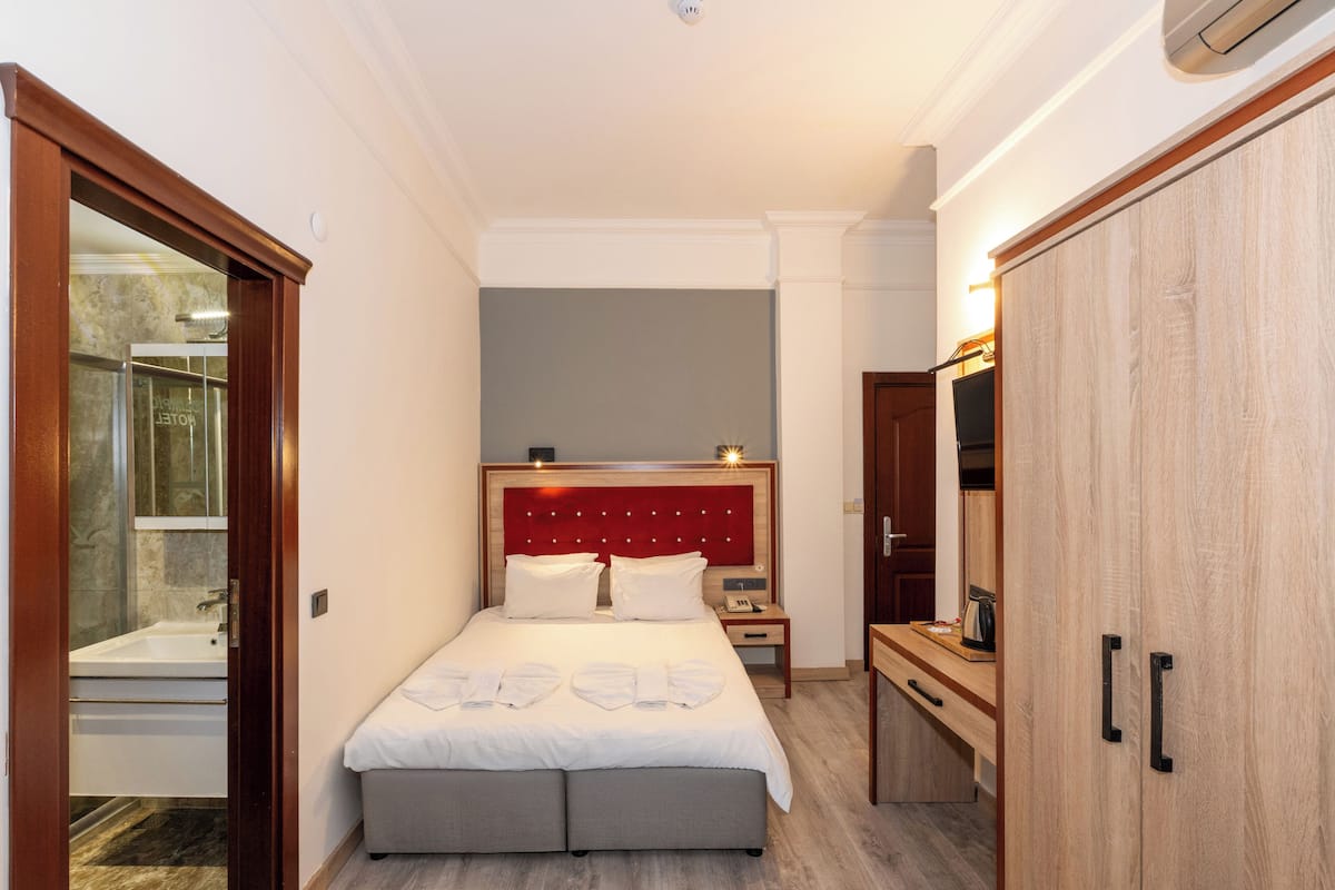 A hotel room with a large bed, a wooden wardrobe, a bedside table, and a bathroom visible through an open door.