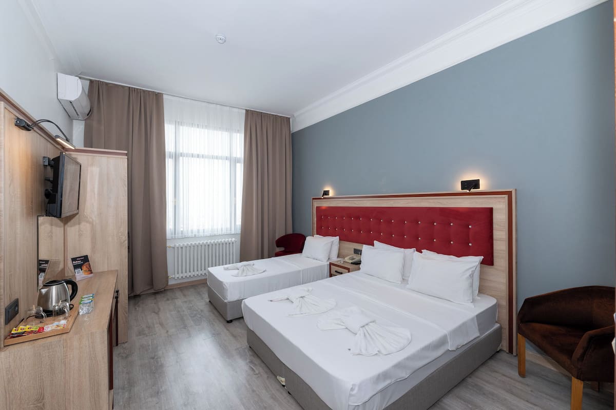 A hotel room with a large bed, a smaller bed, a desk with a kettle, and a chair.