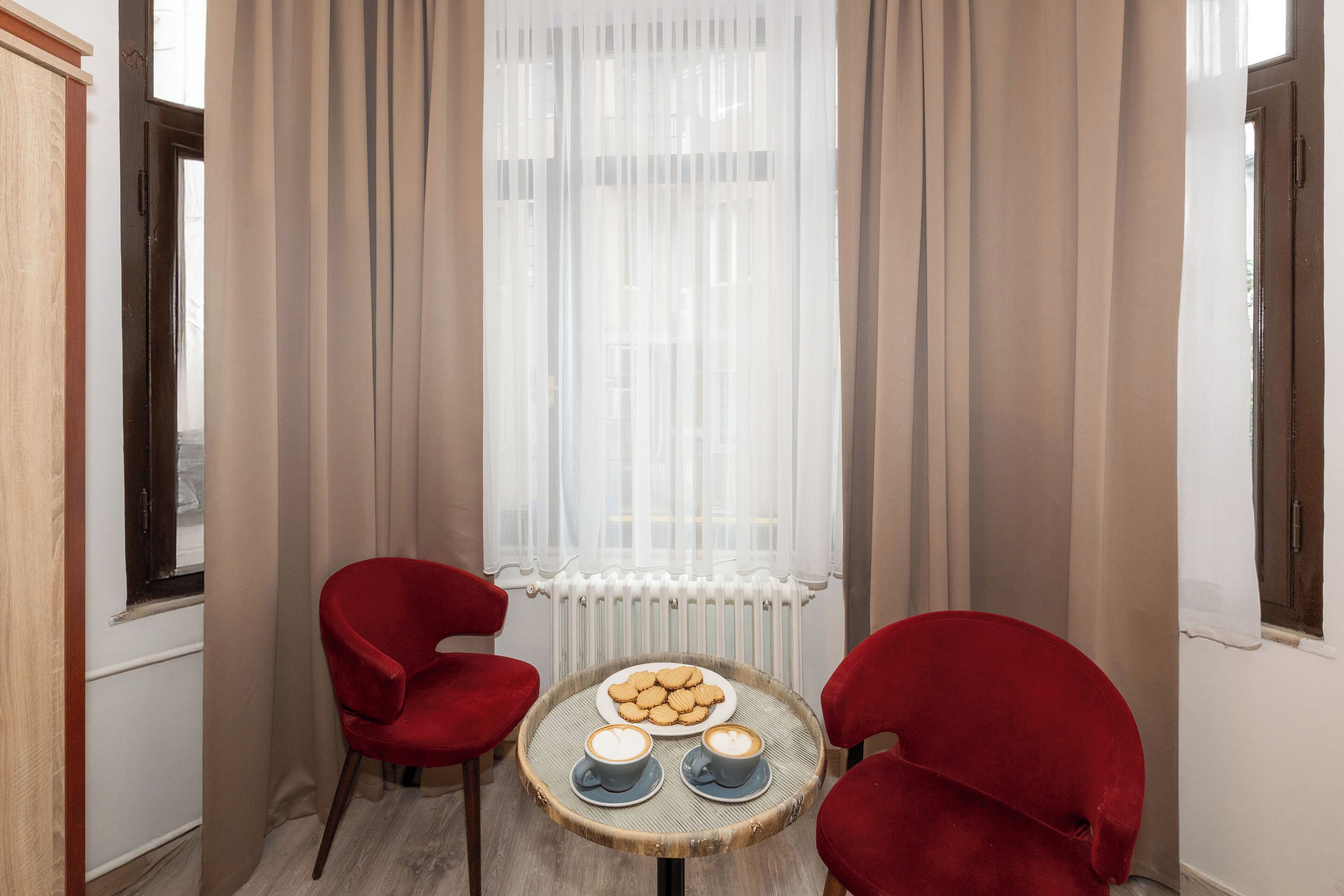 A cozy corner with a round table, two red chairs, a plate of cookies, and two cups of coffee.