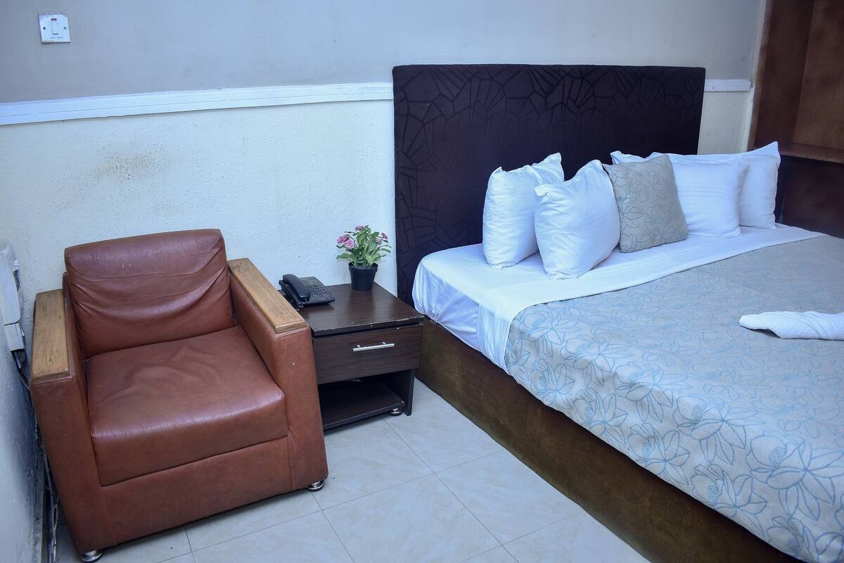 Une chambre à coucher avec un lit, un fauteuil en cuir marron, une table de chevet avec un téléphone et une petite plante.
