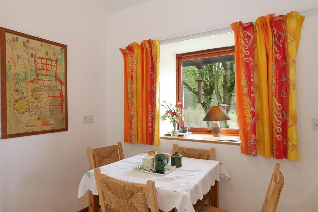 A dining area with a table set for two, a window with curtains, and a painting on the wall.