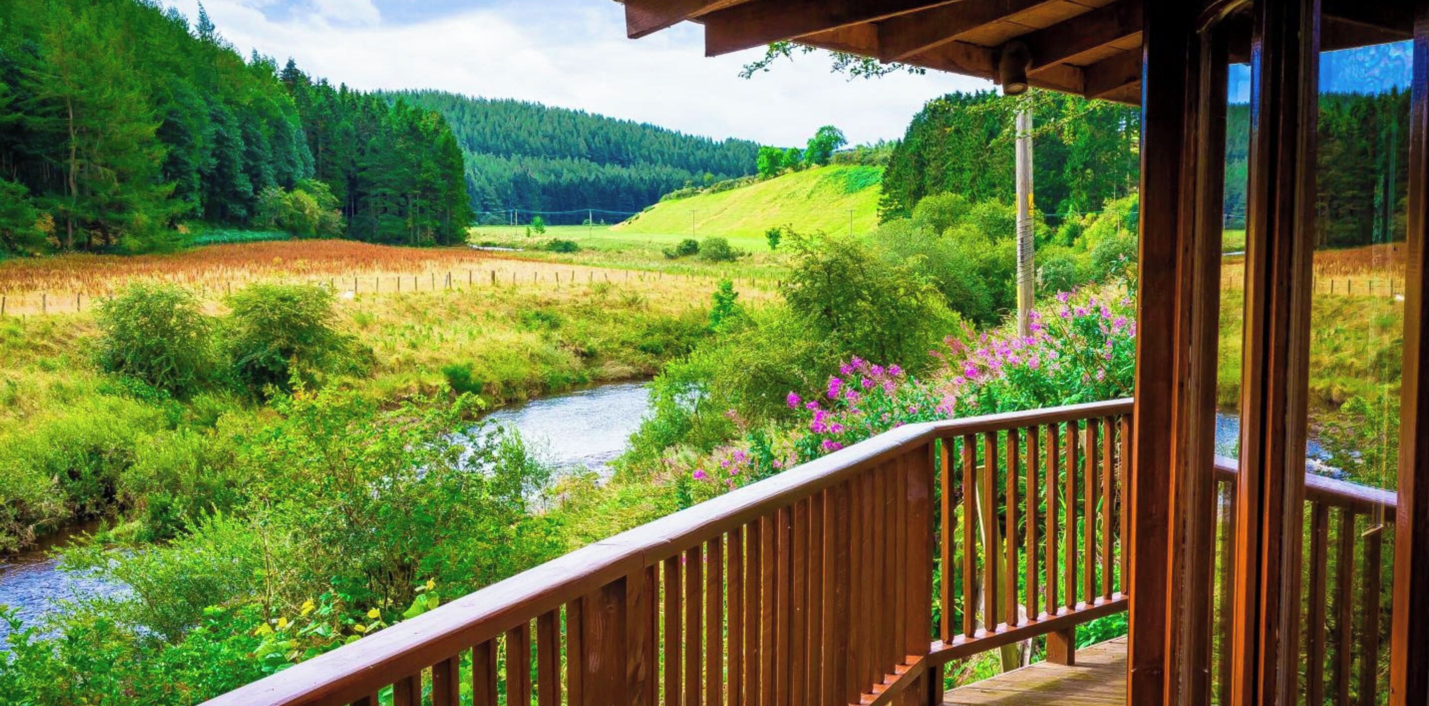A wooden deck overlooking a river with surrounding greenery and hills.