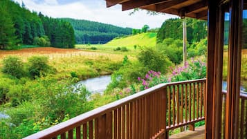 A wooden deck overlooking a river with surrounding greenery and hills.