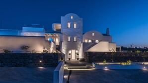 A modern building with a central tower, stone walls, and a well-lit entrance. - White & Co. Exclusive Island Villas (Santorini)