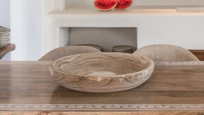 A dining area with a wooden table, a bowl, and a shelf with glasses and a watermelon. - White & Co. Exclusive Island Villas (Santorini)