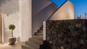 A modern building with a curved staircase leading to a second floor, a stone wall, and a potted plant. - White & Co. Exclusive Island Villas (Santorini)