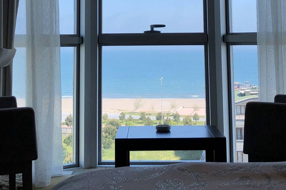 A bay window with a view of the sea, a small table, and two chairs.
