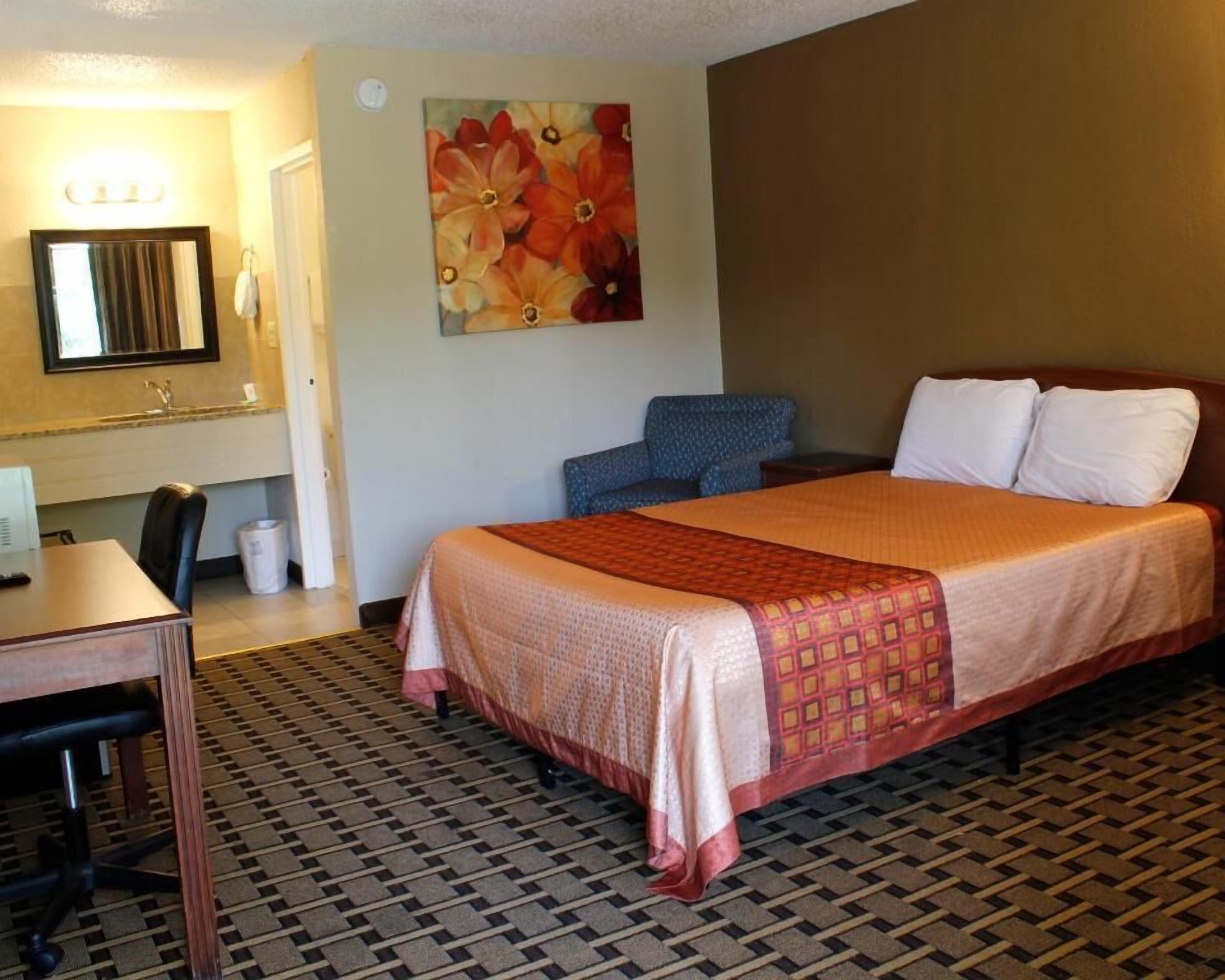 Habitación de hotel con cama, escritorio, silla, espejo y un cuadro en la pared.