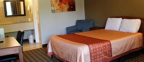 A hotel room with a bed, a desk, a chair, a mirror, and a painting on the wall.