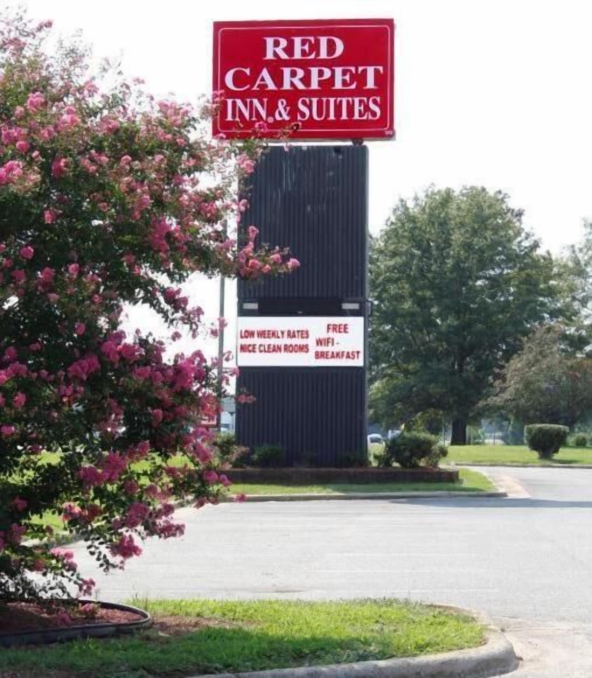 Une enseigne « Red Carpet Inn & Suites » avec une grande banderole rouge et une plus petite enseigne blanche en dessous, faisant la publicité de tarifs hebdomadaires avantageux, d’une connexion Wi-Fi gratuite et du petit-déjeuner.